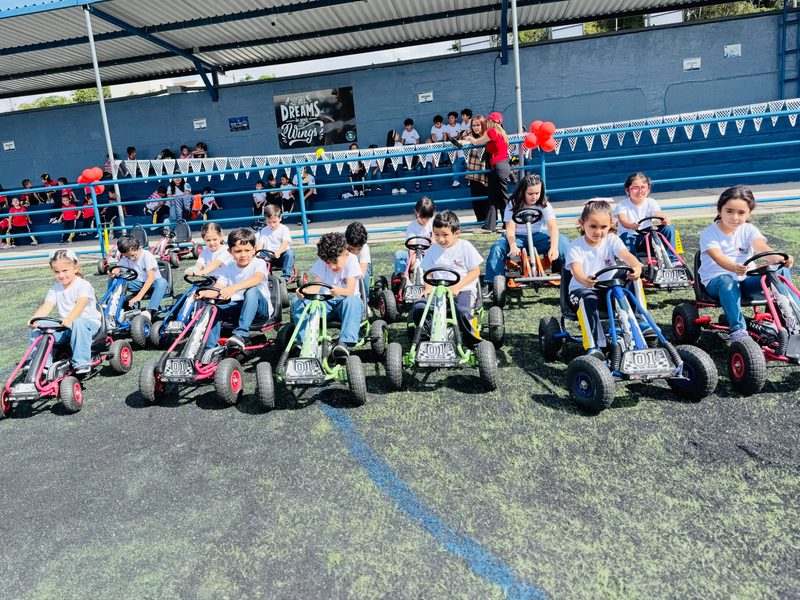 Niños en karts de pedal en la cancha de un colegio durante su fin de ciclo